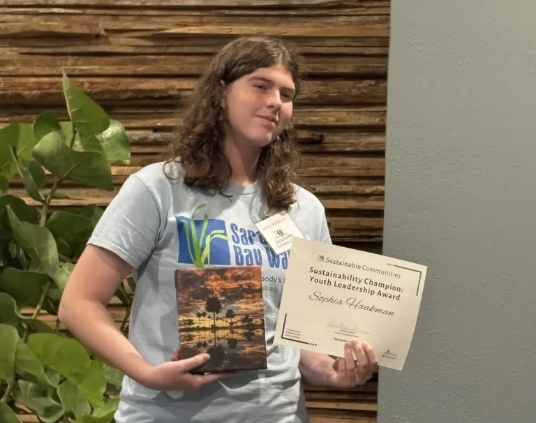 Sophia Haakman holding her award and a print of palm trees and a sunset